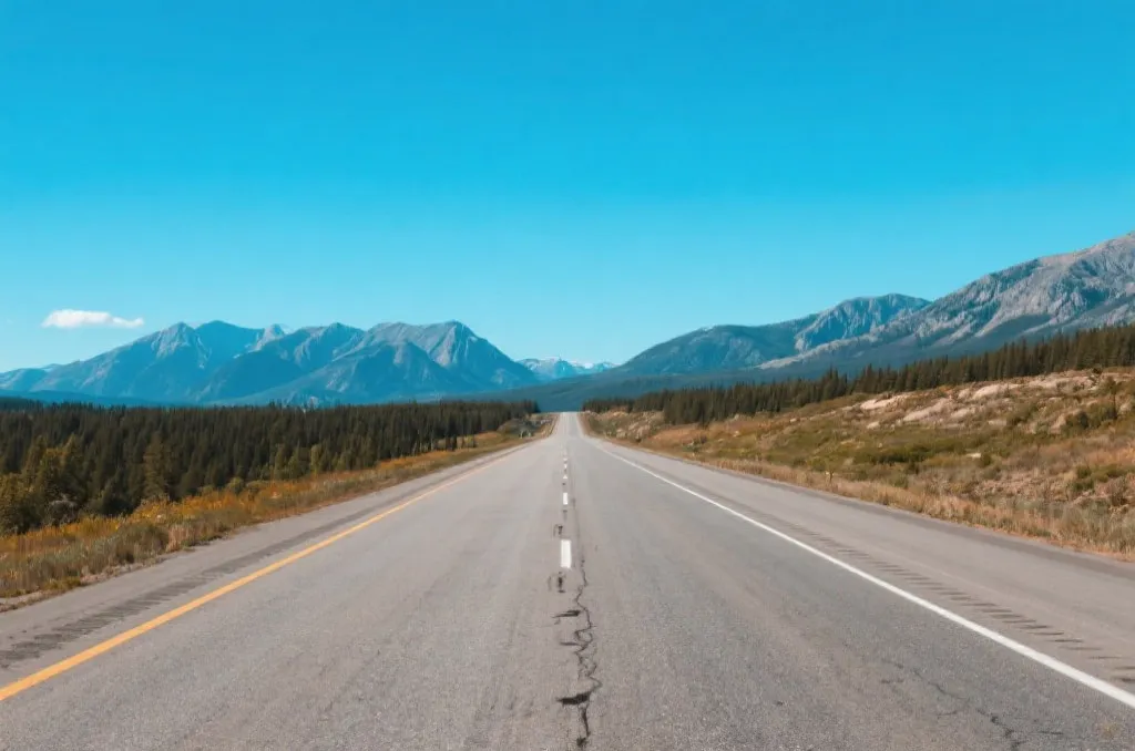 An open scenic highway stretching towards distant mountains under a clear blue sky